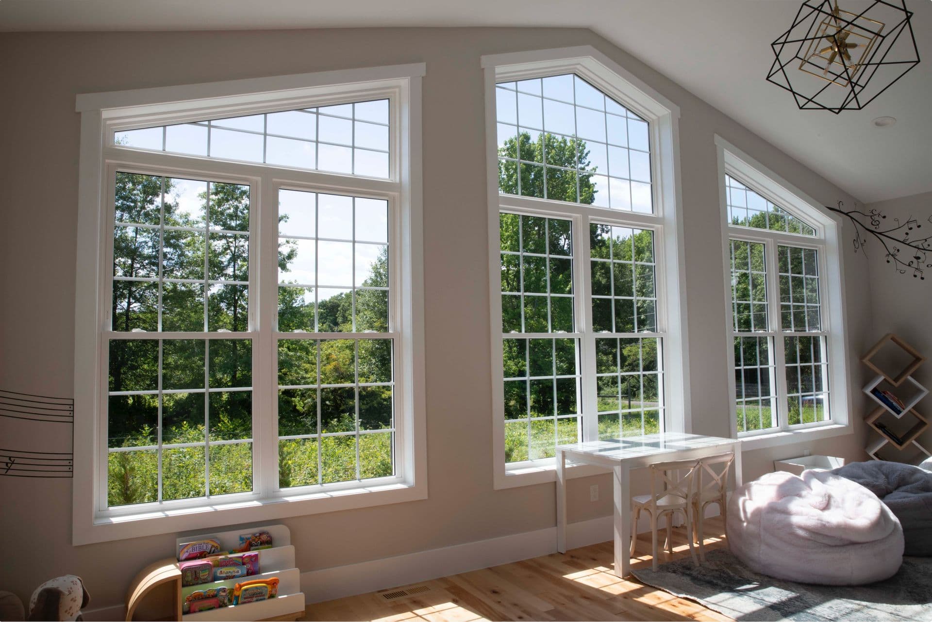 Bright room with large, grid-patterned windows overlooking a lush green landscape. Inside, there's a cozy pink bean bag and a child's table.